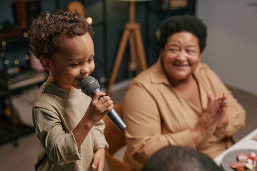 Young child singing into a microphone while a woman claps