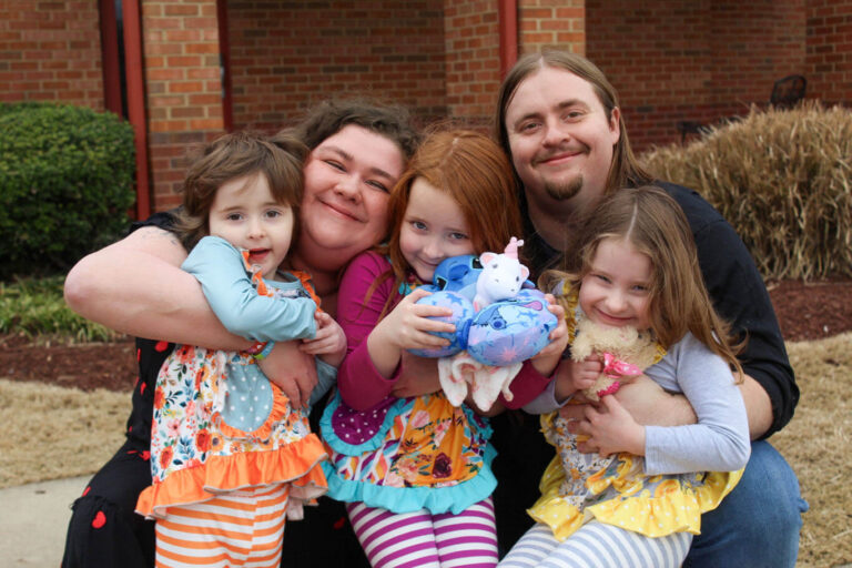 Family of five smiling together outside a brick building